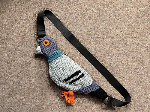 Photo d’un sac type « banane » ou à porter au travers du torse : la pochette représente un pigeon gris clair, gris moyen et noir aux pattes et aux yeux orange et au col vert.